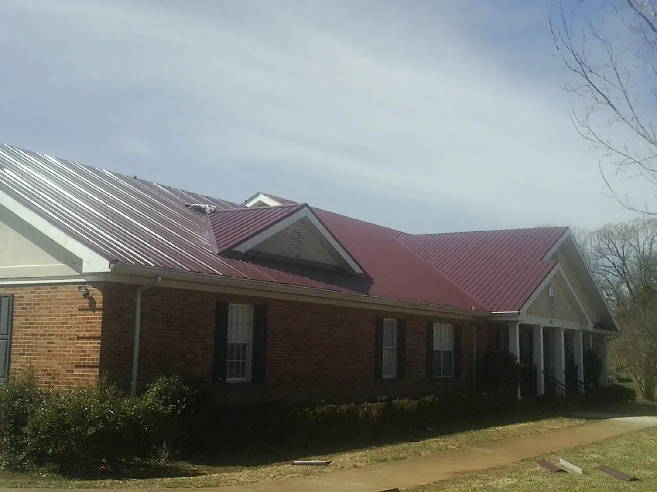 Red metal roof with gabled entries on a long brick building, from a Hail Damage Roof Repair job in Unadilla