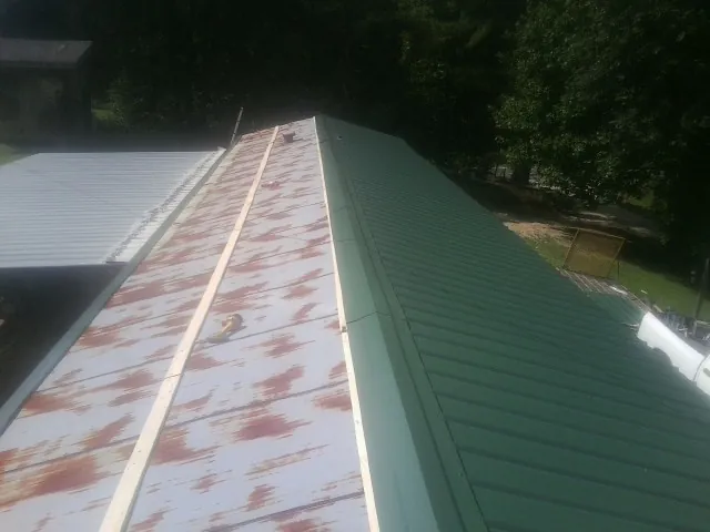 Old rusted panels beside newly installed green metal roofing — Wind Damage Roof Repair by Roofing Brothers in Unadilla