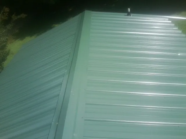 New green metal panels meeting at the ridge of a roof — Flat Roof Repair work by our crew in Unadilla