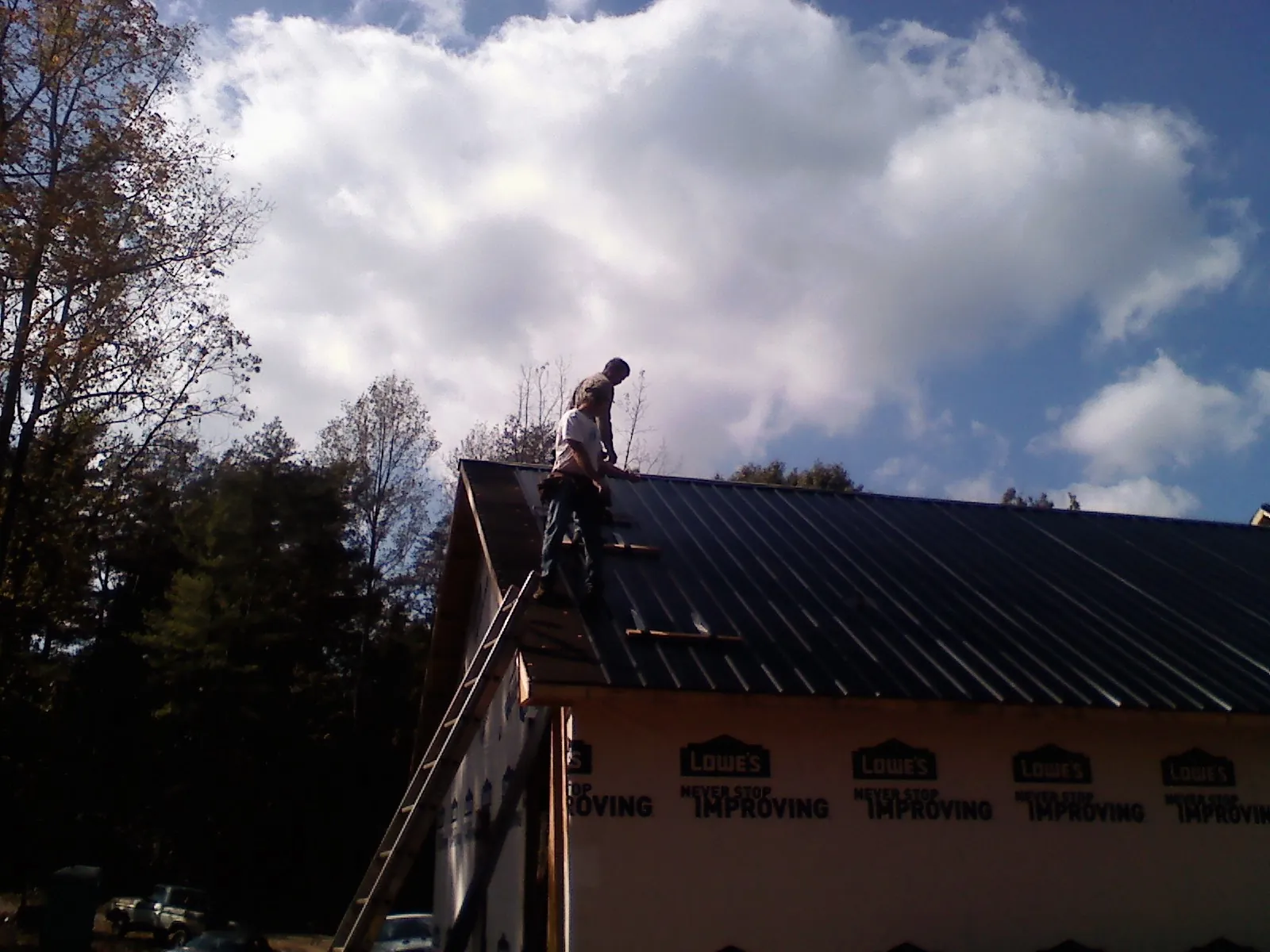 Roofer fastening dark metal panels high against a cloudy sky, from a Roof Inspection job in Unadilla