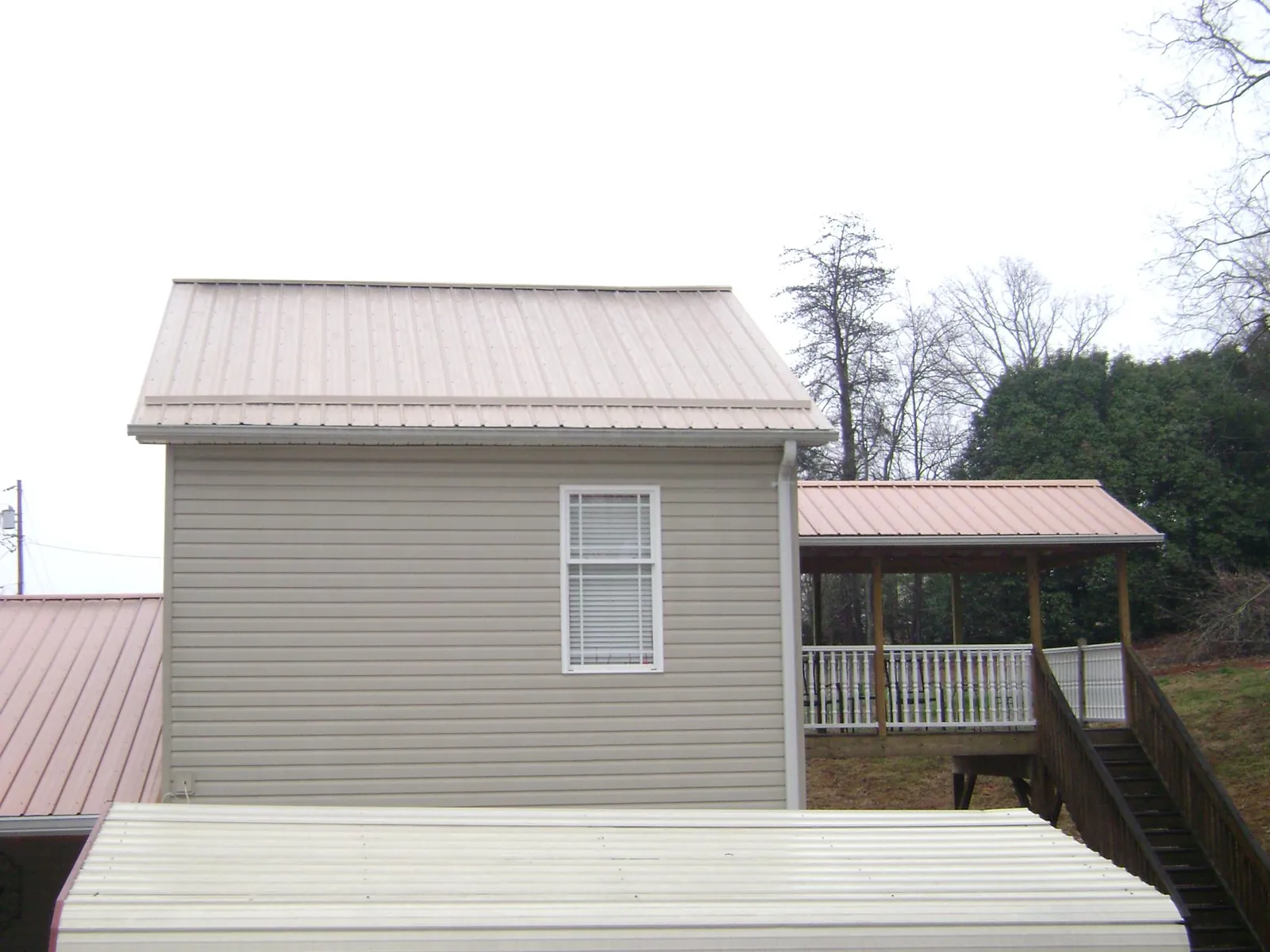 Tan metal roofs on a two story addition and attached porch, from a Roof Replacement job in Unadilla